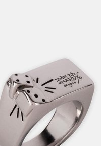 Bague en métal argenté avec un dessus plat, ornée de dés surélevés et d'un motif gravé, finition lisse et anneau légèrement arrondi.