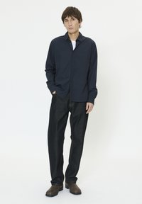 Chemise bleu marine à boutons en coton, associée à un pantalon en jean foncé et des bottes en cuir marron, présentant une coupe décontractée et un design casual.