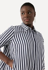 Camicia a righe blu navy e bianca con colletto, chiusura a bottoni e maniche corte, caratterizzata da una vestibilità comoda e tasche laterali.