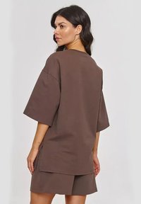 Brązowy, duży t-shirt wykonany z miękkiej tkaniny, z krótkimi rękawami i luźnym krojem, z bocznymi rozporkami dla komfortu i stylu.