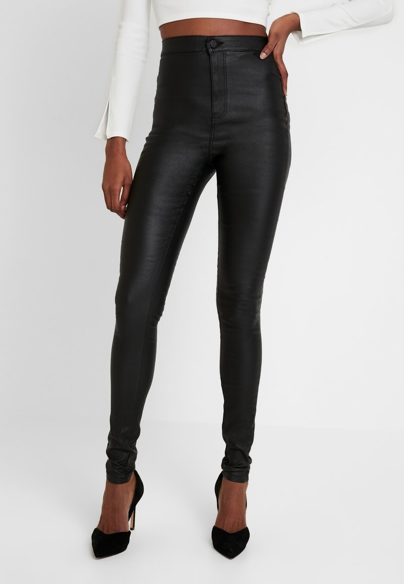 Höga svarta leggings i konstläder med en slät yta, smal passform och knäppning i fronten, kombinerat med svarta högklackade skor.