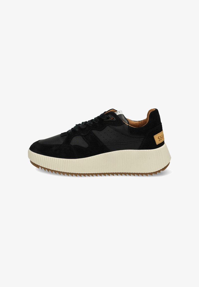 Sneaker noire en mélange de cuir lisse et de daim, avec une semelle en caoutchouc blanche chunky et une accent en brun au niveau du talon.