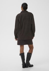 Mørkebrun, ruskindsjakke med en afslappet pasform, lange ærmer og en knappet krave, kombineret med en matchende nederdel og høje sorte læderstøvler.