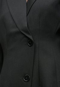 Černé sako s klopou s výstřihem, se dvěma knoflíky a texturovanou tkaninou. Má střih na míru a čisté šicí detaily.