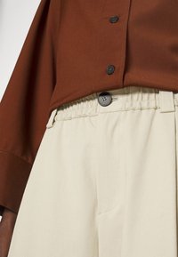 Brązowa koszula na guziki o miękkiej fakturze, zestawiona z kość słoniową spodniami z elastycznym pasem, gładkim wykończeniem i bocznymi kieszeniami.