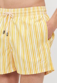 Gelbe und weiße gestreifte Badeshorts mit einem elastischen Bund, Kordelzug und Seitentaschen. Mit einem kleinen gestickten Logo am Saum.