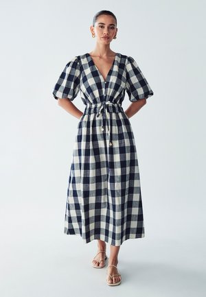 Checked maxi dress in navy and cream with short puff sleeves, fitted waist, and button-down front. Made from lightweight fabric.