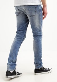 Faded blue jeans with a slim fit and five-pocket design, paired with black high-top sneakers featuring white laces and branding.