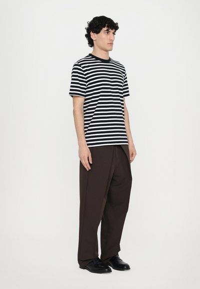Camiseta de rayas en blanco y negro con mangas cortas, combinada con pantalones anchos de color marrón oscuro y zapatos negros. Diseño simple y minimalista.