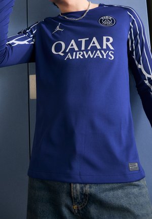 Person trägt ein blaues Langarmtrikot von Paris Saint-Germain mit dem Logo von Qatar Airways, dem Jordan-Brand-Logo und einer silbernen Halskette.