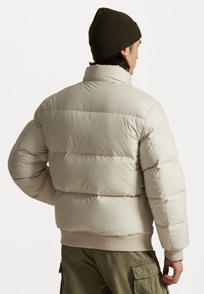 Casaco puffer bege com acolchoamento horizontal, gola alta, bainha canelada e gorro de malha bege, mostrado de costas.