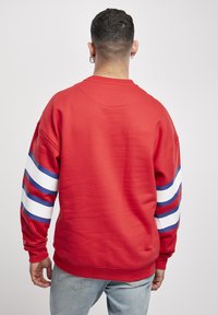 Roter Pullover mit weißen und blauen gestreiften Akzenten an den Ärmeln. Weicher Stoff, lässige Passform, gerippte Bündchen und Bund.