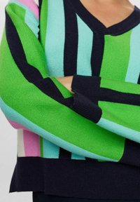 Pleteni pulover z V-izrezom, ki se ponaša z drznimi vertikalnimi črtami v zeleni, svetlo modri, temno modri in roza barvi. Ribani manšeti in rob. Mehak tekstura.