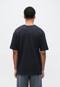 T-shirt preta de algodão com mangas curtas e decote redondo, apresentando um ajuste descontraído e textura suave, vista por trás.