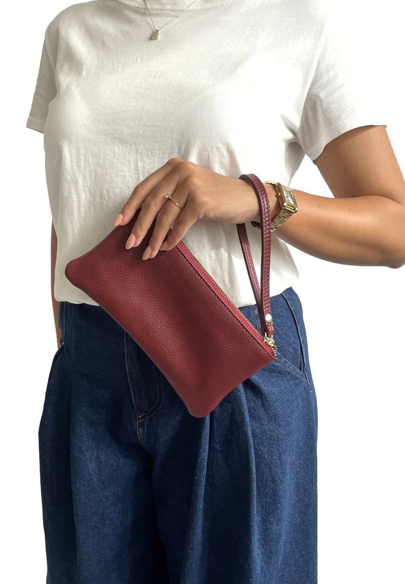 Borsa a mano in pelle rossa con finitura testurizzata, chiusura con zip e tracolla, appoggiata su una t-shirt bianca e pantaloni in denim.