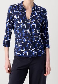 Camisa de botones azul marino con un patrón abstracto en blanco y azul, diseño de cuello y mangas tres cuartos, confeccionada en una tela suave y lisa.