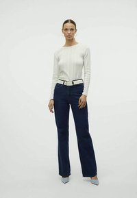 Valkoinen ribattu pitkähihais sweater, joka on yhdistetty tummansinihin korkeavyötäröisiin farkkuihin ja valkoiseen vyöhön. Mallilla on päällään vaaleansiniset korkokengät.