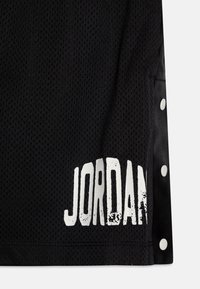 Black mesh fabric basketball jersey with white "JORDAN" text. Side snap detailing and breathable texture. Lightweight design.