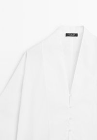 Biała koszula zapinana na guziki z szerokim kołnierzem i długimi rękawami, z metką marki "Massimo Dutti" wewnątrz dekoltu.