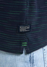 Camisa de punto azul marino con patrones de rayas verdes y moradas. Incluye una etiqueta azul con texto blanco que dice "Petrol Ind" en el dobladillo.