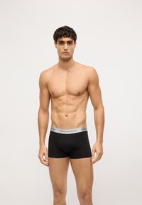 Boxer cortos de algodón negros con una cinturilla elástica plateada que presenta el logotipo "TOMMY HILFIGER", textura suave y diseño ajustado.