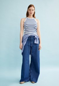 Gestreepte tanktop in wit en blauw met een brede blauwe jeans, voorzien van een gestrikt, gestreept shirt om de taille. Gladde stof, casual uitstraling.