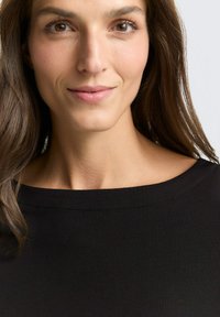 Zwarte top met een brede halslijn, zachte textuur en gladde stof. Close-up van een gezicht met bruine ogen en bruin haar.