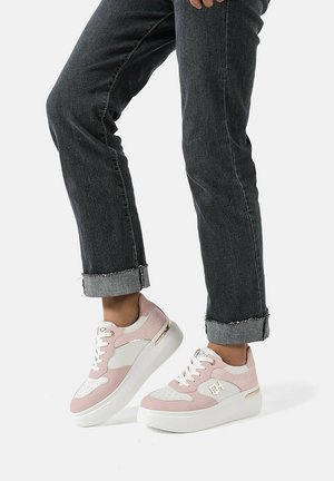 Sneaker rosa e bianchi con una parte superiore testurizzata, sottili accenti dorati e una suola bianca spessa, abbinate a jeans scuri arrotolati.