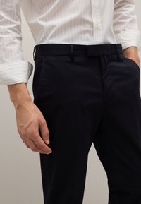 Navyblauwe katoenen broeken met een platte voorkant, zijzakken en een gladde textuur. G gedragen met een wit overhemd met streepjes die de tailleband toont.