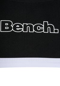 Haut de sport en tissu noir avec un logo "Bench." blanc bien visible. Encolure ronde avec un ourlet blanc en bas. Texture lisse.