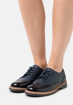 Chaussures à lacets en cuir bleu marine avec embout brillant noir, détails brogue et finition texturée. Semelle en caoutchouc avec couture marron clair.