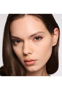 Primo piano di una persona con capelli lisci, castano scuro. Pelle liscia con trucco leggero, colore naturale delle labbra e trucco occhi delicato.