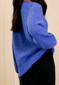Pull bleu surdimensionné en maille avec une finition texturée et des manches longues, doté d'un col rond et d'un ourlet légèrement asymétrique.