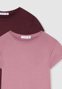 Dwie koszulki w widoku ułożonym jedna na drugiej: jedna bordowa, a druga jasnoróżowa, obie mają okrągły dekolt i krótkie rękawy, wykonane z gładkiego materiału.