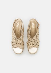 Sandali slingback intrecciati in oro con punta metallica lucida; design aperto con fibbie incrociate e una piccola chiusura regolabile.
