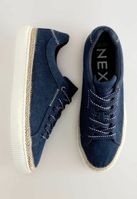 Blå denimskor med vita gummisulor, utrustade med kontrasterande vita sömmar och en flätad jute Kant längs sulan, med runda snören.