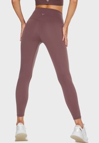 Leggings a vita alta di un profondo colore malva, realizzati in tessuto elastico, con una texture liscia e un design senza cuciture, abbinati a scarpe da ginnastica bianche.