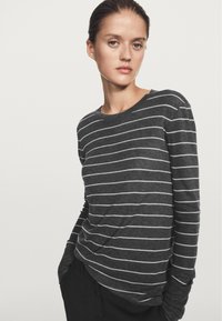 Długi rękaw, pasiasta koszulka w ciemnoszarym kolorze z białymi poziomymi paskami. Wykonana z miękkiego materiału, o luźnym fasonie i okrągłym dekolcie.