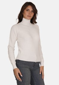 Maglione a collo alto lavorato a maglia in crema, con una texture a coste e un design attillato, abbinato a jeans grigio scuro. Semplice e versatile.