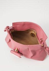 Pink leather handbag open, showing beige fabric interior with zippered pocket and round leather patch detail inside.