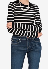 Raitaraitainen mustavalkoinen ribbipaita, jossa on pitkät hihat, yhdistettynä tummansinisiin farkkuihin, joissa on etutaskut ja napitus.