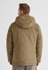 Braune Kapuzenjacke mit einer glatten, wildlederartigen Textur. Sie hat einen lockeren Schnitt und ein schlichtes Design, mit sichtbaren Nähten entlang der Säume.