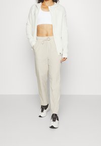 Lätt, krämfärgad zip-up huvtröja med huva, tillsammans med beige dragkedjebyxor. Vita och svarta sneakers fulländar outfiten.