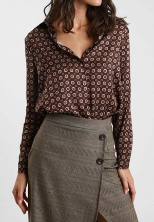 Blusa marrone a fantasia con colletto, caratterizzata da disegni geometrici in tonalità chiare, abbinata a una gonna a quadri texturizzata con bottoni.