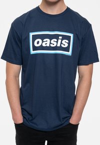 Navy blue cotton t-shirt featuring a white "oasis" logo in a black rectangle outlined in light blue. Short sleeves, relaxed fit.