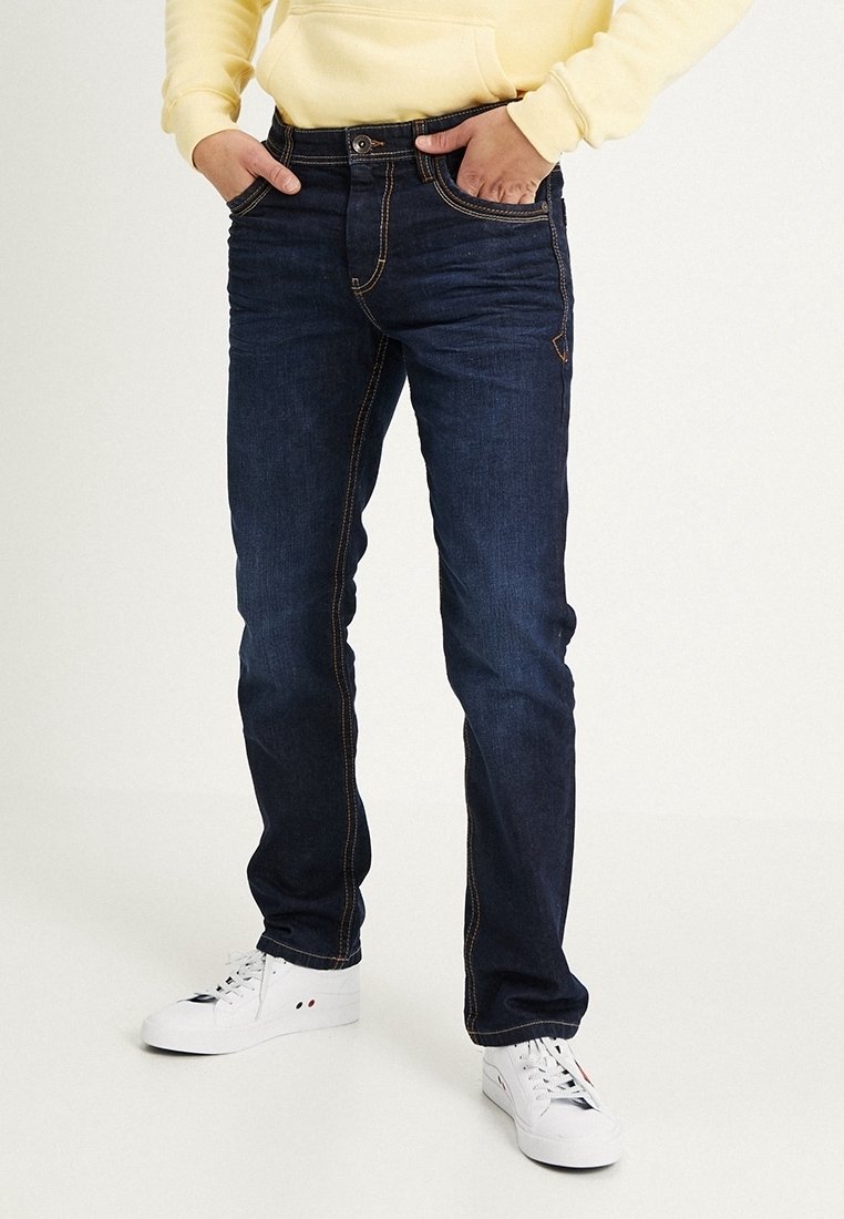 Jeans de mezclilla azul oscuro con costuras naranjas, que presentan un diseño clásico de cinco bolsillos y un corte recto. Se llevan con zapatillas blancas.