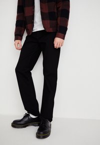 Black denim pants paired with a maroon and navy plaid button-up jacket. The shoes are black leather with yellow stitching and thick soles.