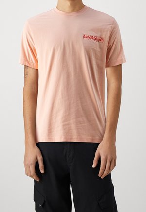 Jasnoróżowa bawełniana koszulka z krótkim rękawem, z małym czerwonym logo na wysokości kieszonki na piersi oraz luźnym krojem.