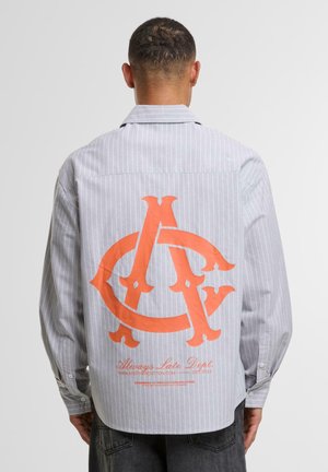 Striped long-sleeve shirt in light gray with an orange oversized logo design on the back, featuring a buttoned cuff and casual fit.