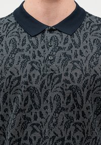 Μπλε ρουά πόλο πουκάμισο με υφή σχεδίου από σκούρα φύλλα, με ριμπ λαιμόκοψη και τριπλή σειρά κουμπιών. Μαλακό ύφασμα με κλασική εφαρμογή.